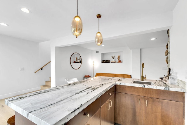 kitchen featuring sink, kitchen peninsula, pendant lighting, and light hardwood / wood-style floors