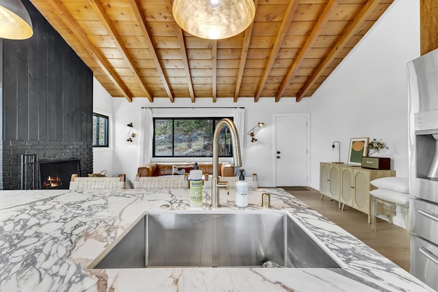 kitchen with lofted ceiling with beams, light stone countertops, sink, and a brick fireplace