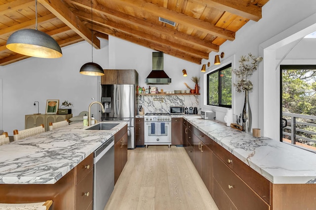 kitchen featuring wall chimney range hood, hanging light fixtures, appliances with stainless steel finishes, light hardwood / wood-style flooring, and light stone counters