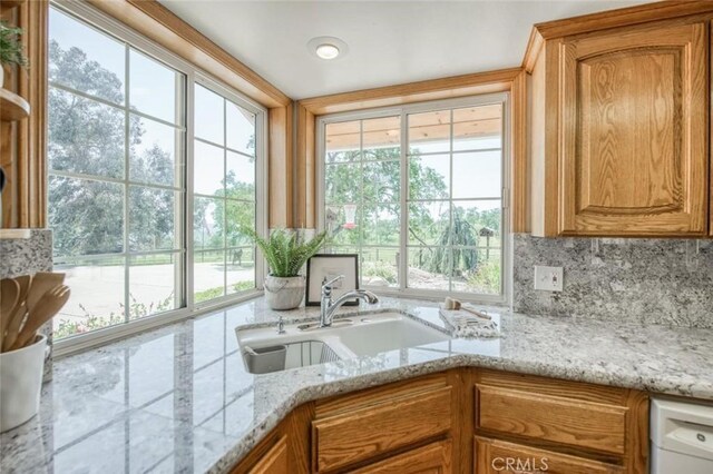 18486 Tollhouse Rd, Clovis, CA 93619 - kitchen with a sink, brown cabinets, backsplash, and light stone counters