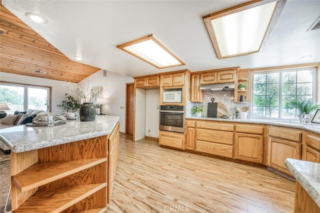 kitchen with light stone countertops, stainless steel oven, white microwave, light hardwood / wood-style floors, and lofted ceiling