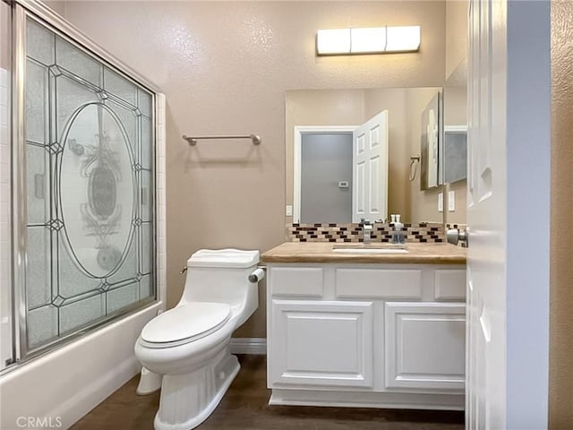 full bathroom with toilet, wood finished floors, vanity, combined bath / shower with glass door, and backsplash