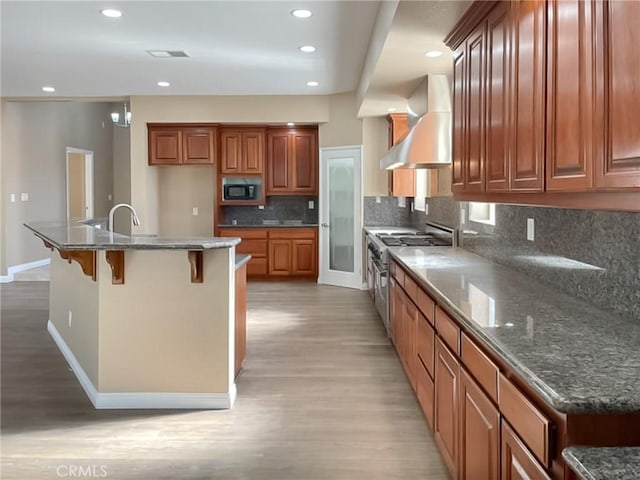 kitchen with a kitchen island, black microwave, dark stone countertops, high end stainless steel range oven, and wall chimney exhaust hood