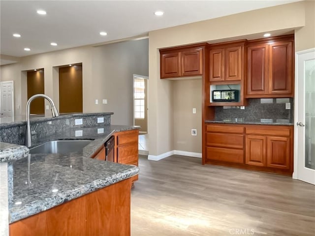 kitchen with dishwasher, sink, dark stone countertops, backsplash, and light hardwood / wood-style flooring