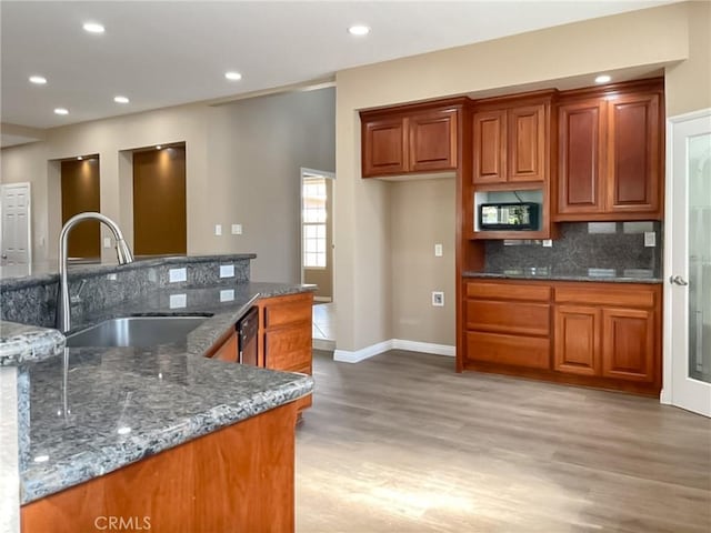 kitchen featuring a sink, tasteful backsplash, brown cabinets, and dark stone countertops