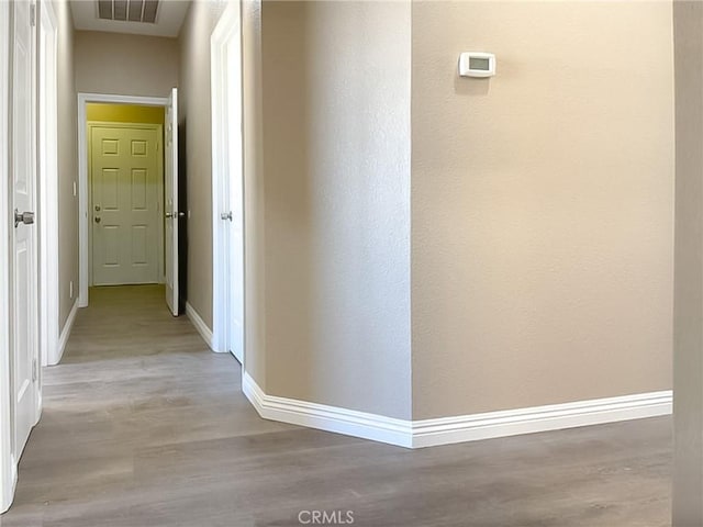 corridor with light wood finished floors, baseboards, and visible vents