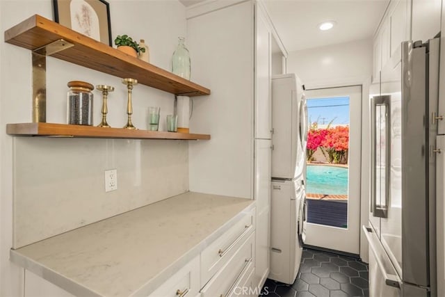 interior space featuring stacked washing maching and dryer, light stone counters, dark tile patterned flooring, white cabinetry, and stainless steel refrigerator