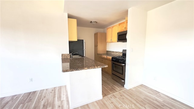 kitchen featuring stainless steel appliances, light hardwood / wood-style flooring, kitchen peninsula, and light brown cabinets