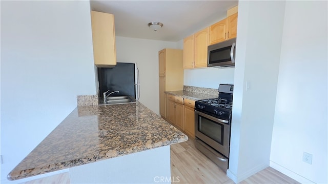 kitchen with kitchen peninsula, light brown cabinetry, light wood-type flooring, stainless steel appliances, and sink