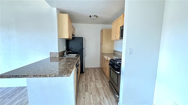 kitchen featuring refrigerator, kitchen peninsula, a breakfast bar area, black gas range oven, and light hardwood / wood-style flooring