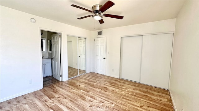 unfurnished bedroom featuring ceiling fan, multiple closets, light wood-type flooring, and ensuite bath