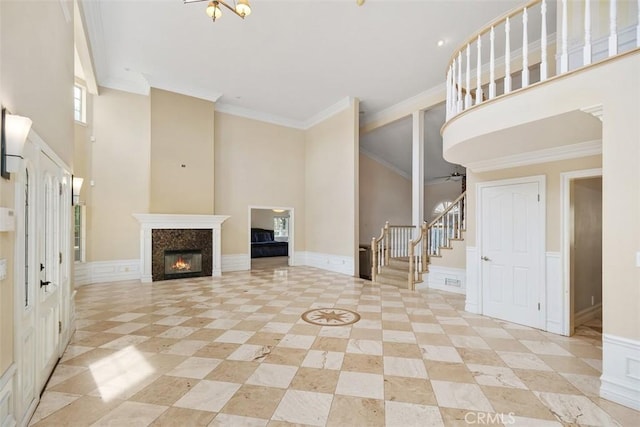 unfurnished living room featuring a towering ceiling, ceiling fan, and ornamental molding