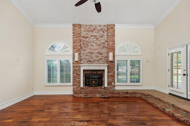 unfurnished living room featuring wood-type flooring, a brick fireplace, ceiling fan, and crown molding