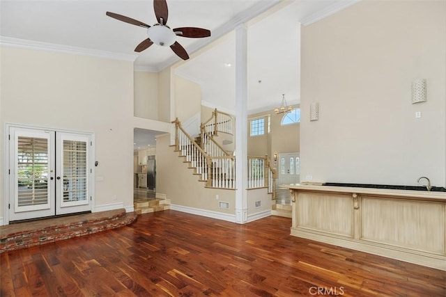 unfurnished living room with french doors, dark wood-type flooring, crown molding, a towering ceiling, and ceiling fan with notable chandelier