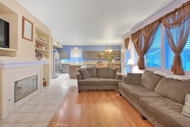 living room featuring a fireplace, light hardwood / wood-style flooring, built in features, and a notable chandelier