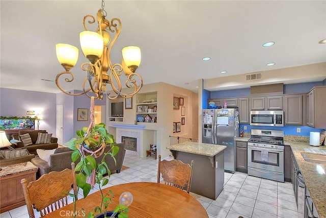 kitchen with a tile fireplace, stainless steel appliances, a notable chandelier, decorative light fixtures, and a kitchen island