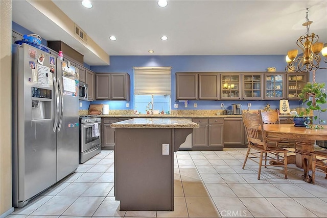 kitchen featuring light stone countertops, stainless steel appliances, decorative light fixtures, a center island, and light tile patterned flooring