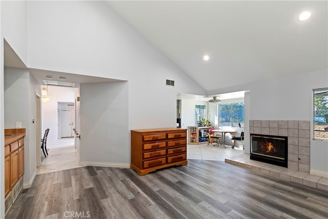 living room with a healthy amount of sunlight, a tiled fireplace, high vaulted ceiling, and light wood-type flooring