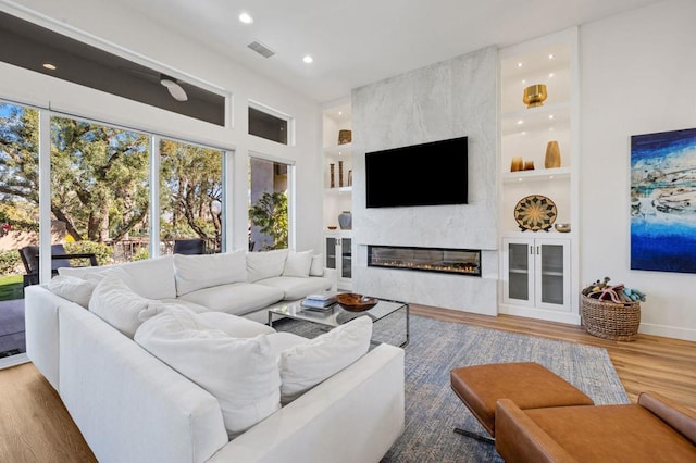 living room featuring built in shelves, a large fireplace, and wood-type flooring