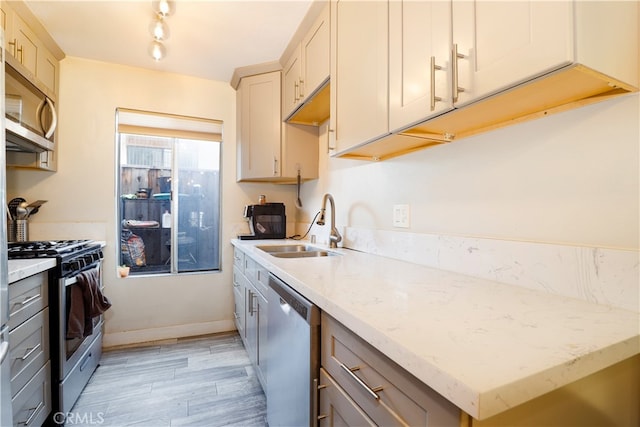 kitchen featuring light stone counters, light hardwood / wood-style flooring, sink, gray cabinets, and stainless steel appliances