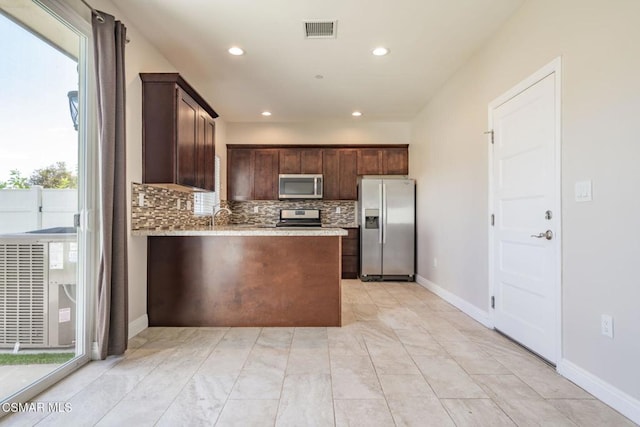 kitchen featuring kitchen peninsula, dark brown cabinets, stainless steel appliances, backsplash, and sink