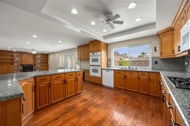 kitchen with sink, dark hardwood / wood-style flooring, backsplash, white appliances, and a tray ceiling