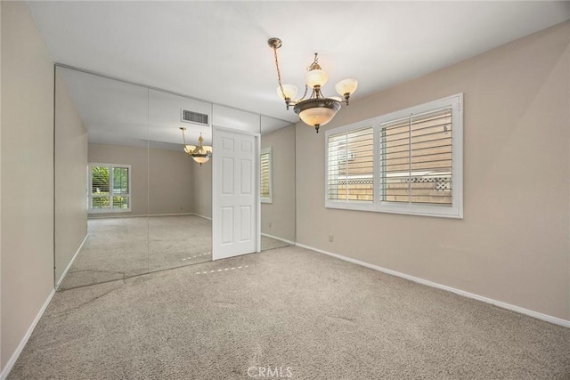 empty room featuring light colored carpet and an inviting chandelier