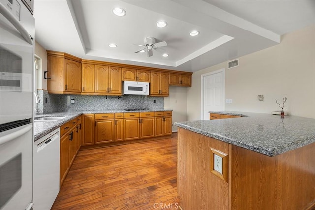 kitchen with white appliances, a raised ceiling, ceiling fan, light hardwood / wood-style floors, and kitchen peninsula