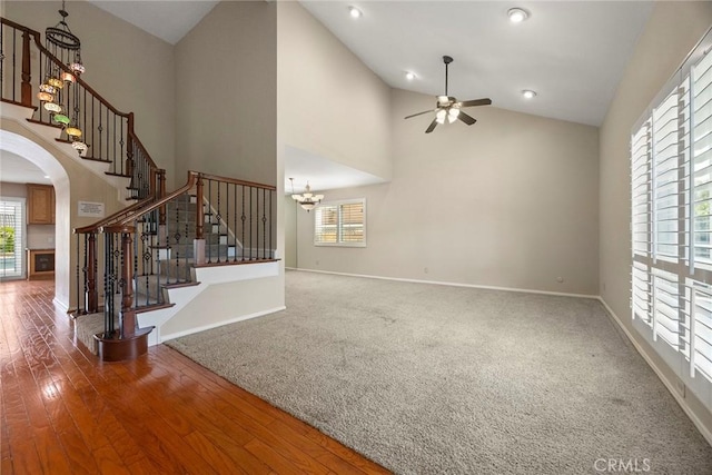 unfurnished living room with ceiling fan with notable chandelier, wood-type flooring, and high vaulted ceiling