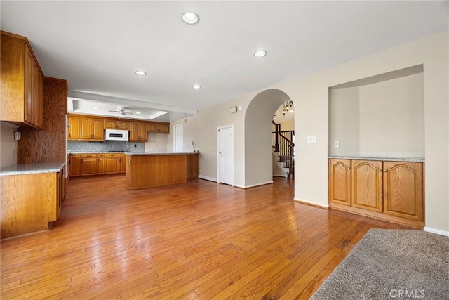 kitchen with light wood-type flooring, a kitchen island, ceiling fan, and backsplash