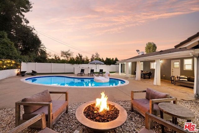 pool at dusk featuring an outdoor living space with a fire pit and a patio