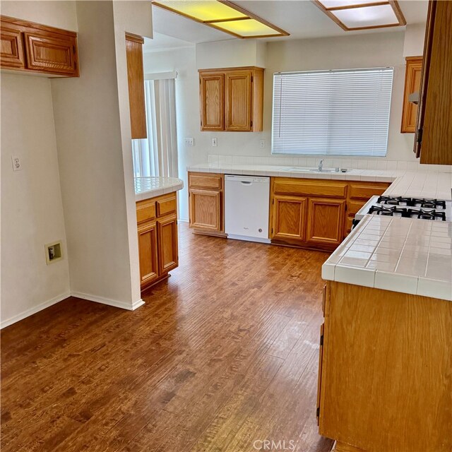 kitchen with white appliances, wood-type flooring, sink, and tile counters