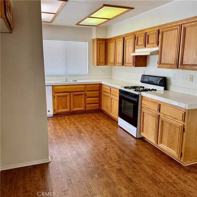 kitchen with tasteful backsplash, wood-type flooring, tile counters, sink, and white appliances