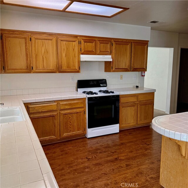 kitchen featuring tile countertops, dark hardwood / wood-style floors, a skylight, sink, and white gas range oven