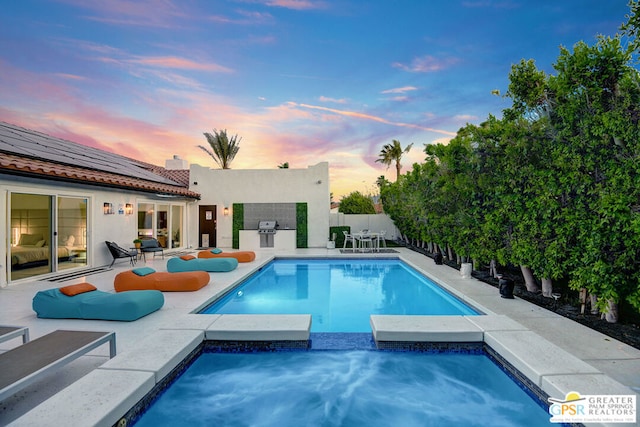 pool at dusk featuring a patio area and an in ground hot tub