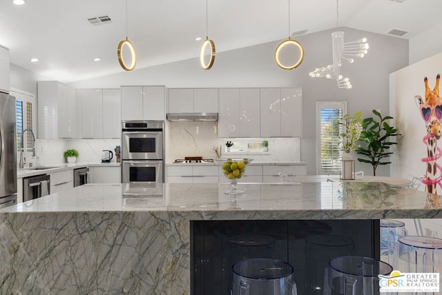 kitchen featuring pendant lighting, lofted ceiling, appliances with stainless steel finishes, light stone counters, and white cabinetry