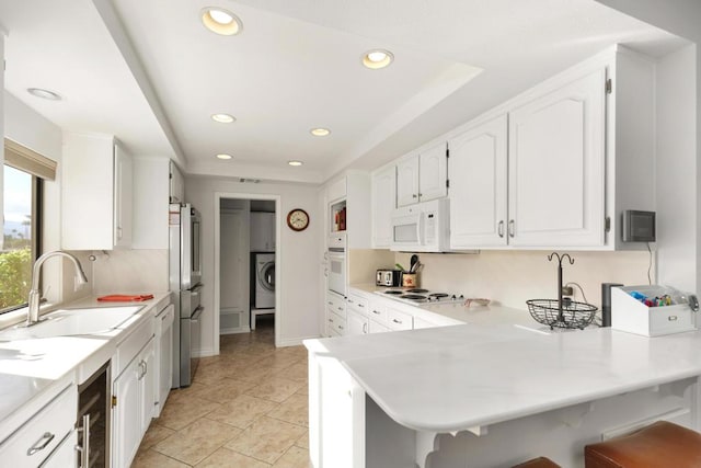 kitchen with white cabinetry, sink, kitchen peninsula, white appliances, and washer / dryer