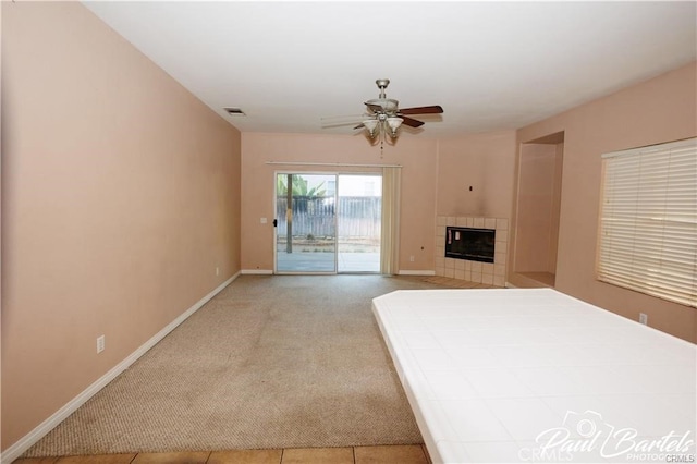 unfurnished bedroom with a tile fireplace, access to exterior, light colored carpet, and ceiling fan