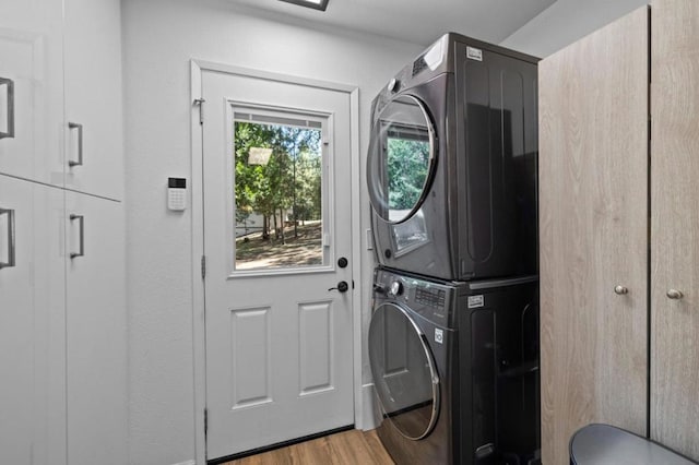 laundry room with stacked washing maching and dryer, cabinets, and light wood-type flooring