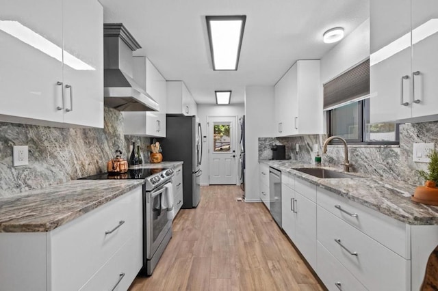 kitchen featuring wall chimney exhaust hood, sink, stainless steel appliances, and white cabinetry