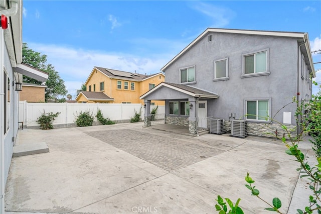 rear view of property with stone siding, central AC unit, a fenced backyard, and stucco siding