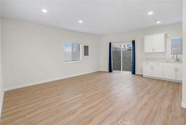 unfurnished living room featuring light wood-type flooring, baseboards, a sink, and recessed lighting