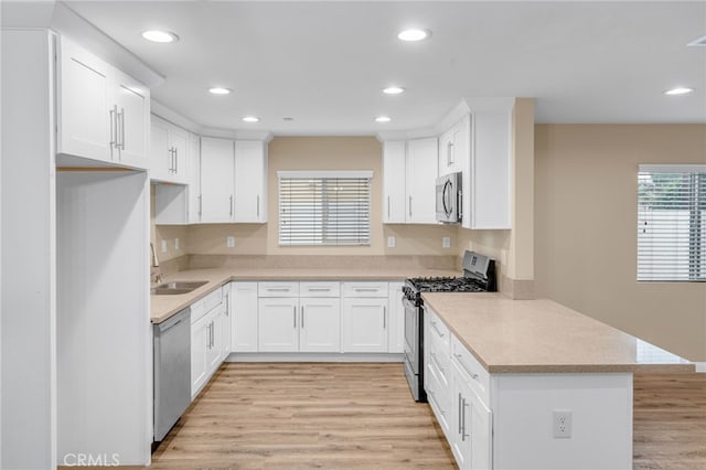 kitchen with a peninsula, a sink, white cabinets, light countertops, and appliances with stainless steel finishes