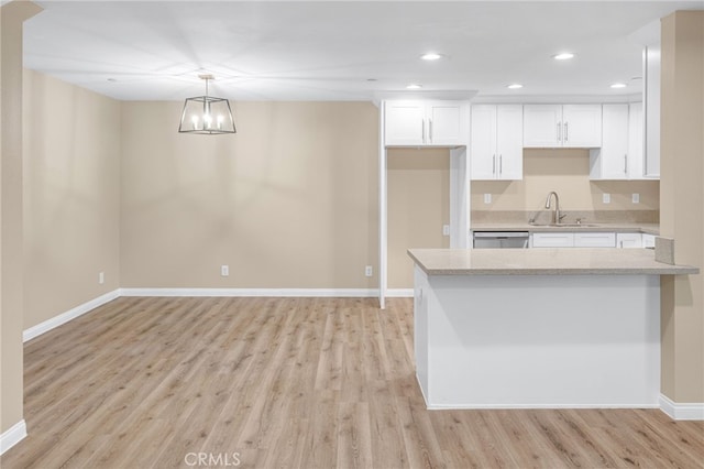 kitchen featuring decorative light fixtures, light countertops, light wood-style floors, white cabinets, and a sink