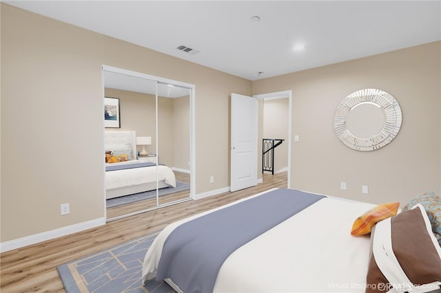 bedroom with a closet, wood finished floors, visible vents, and baseboards