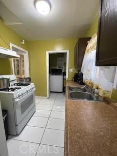 kitchen featuring dark brown cabinetry, washer / dryer, sink, white range with gas stovetop, and light tile patterned floors