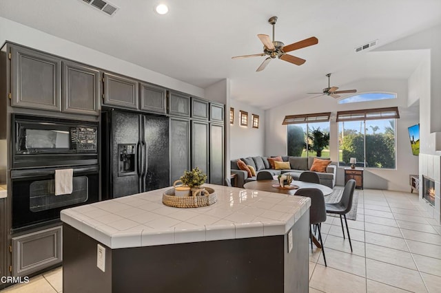 kitchen with tile countertops, a center island, lofted ceiling, black appliances, and light tile patterned floors