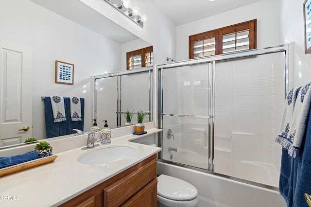 full bathroom featuring vanity, combined bath / shower with glass door, and toilet