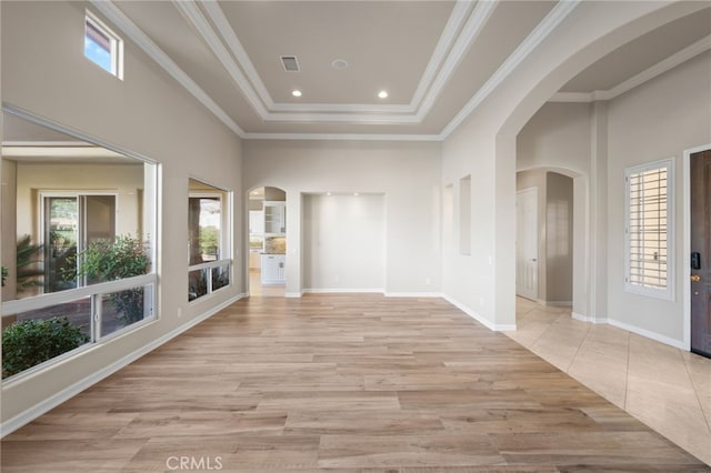 interior space featuring a towering ceiling, light wood-type flooring, and crown molding