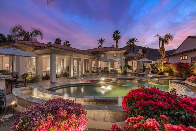 pool at dusk featuring a patio area and an in ground hot tub